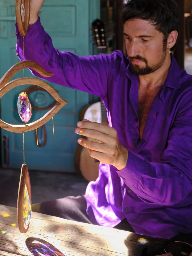 Arihant Ortega holding up a wooden eye pendant with a crystal in a turquoise doorway