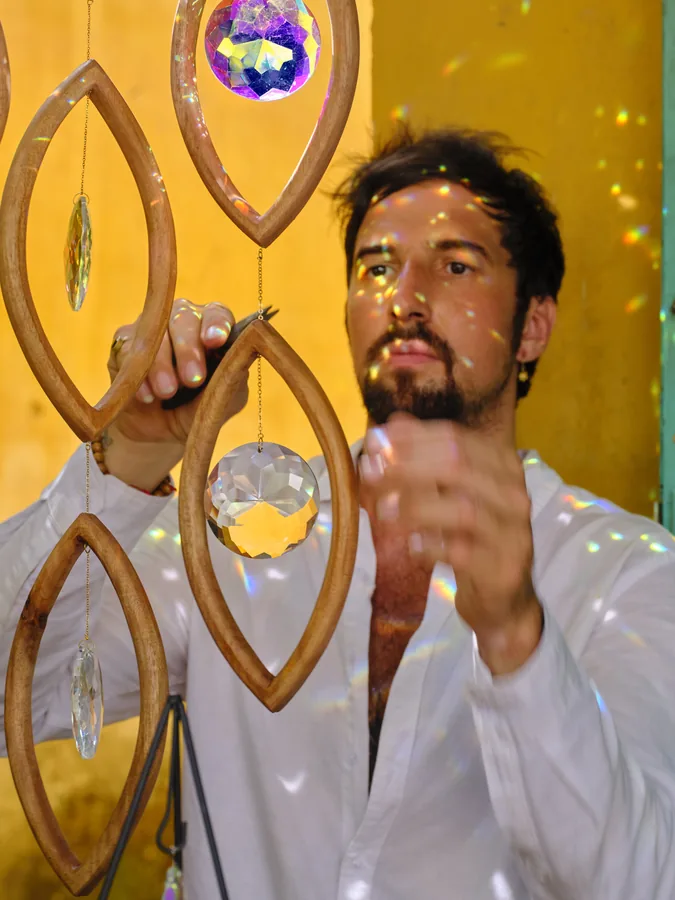 Arihant Ortega among hanging wooden eye pieces, a crystal catching the light in his hand