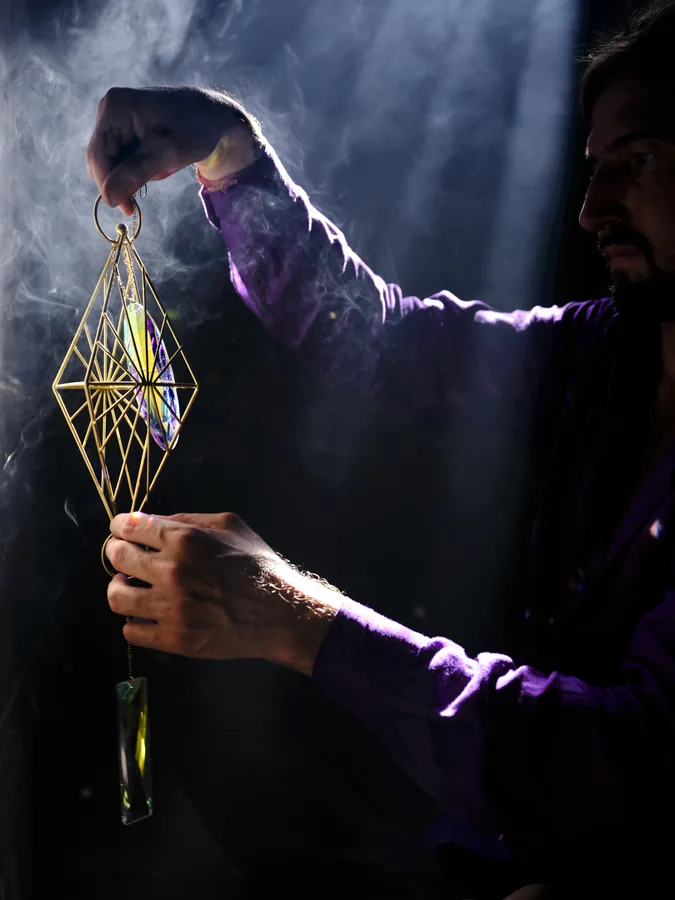 A brass wire pyramid pendant held up in a dark, smoky room, lit from one side