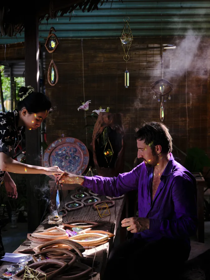 Arihant Ortega at a workbench in the studio at dusk, wood pieces and hanging works around him